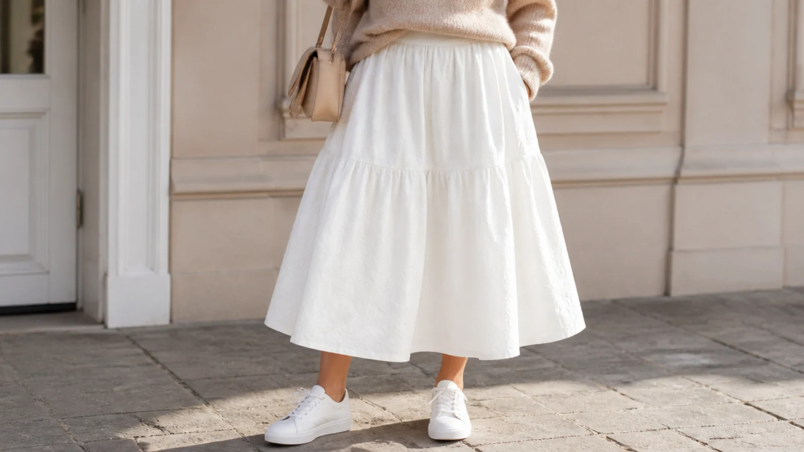 Faceless waist-down shot of clean white leather sneakers worn with a white midi skirt
