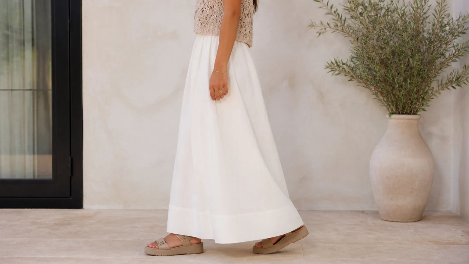 Faceless side view of a white maxi skirt hem sitting half an inch above the floor over a platform sandal