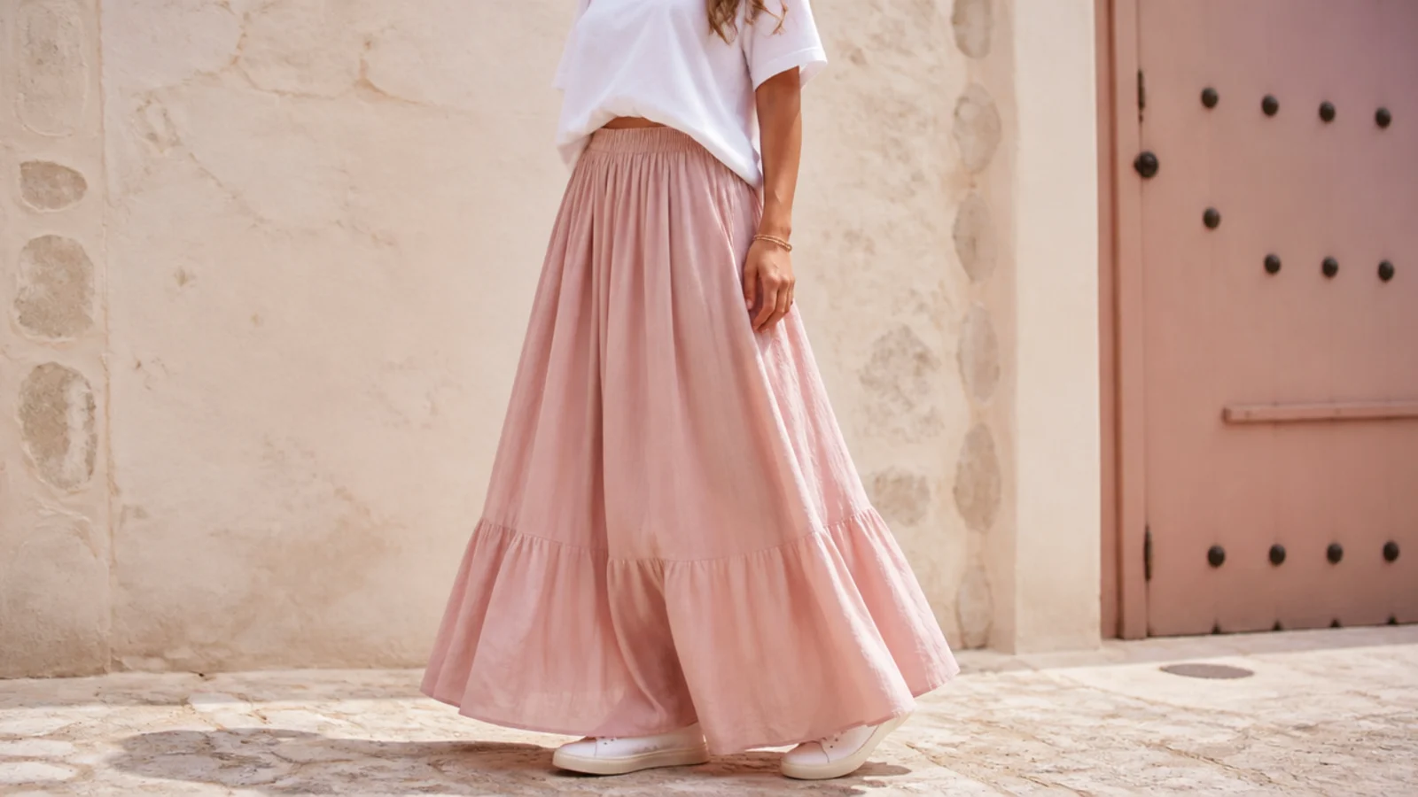 Faceless full-length shot of a flowing maxi skirt with a low white leather sneaker peeking out at the hem