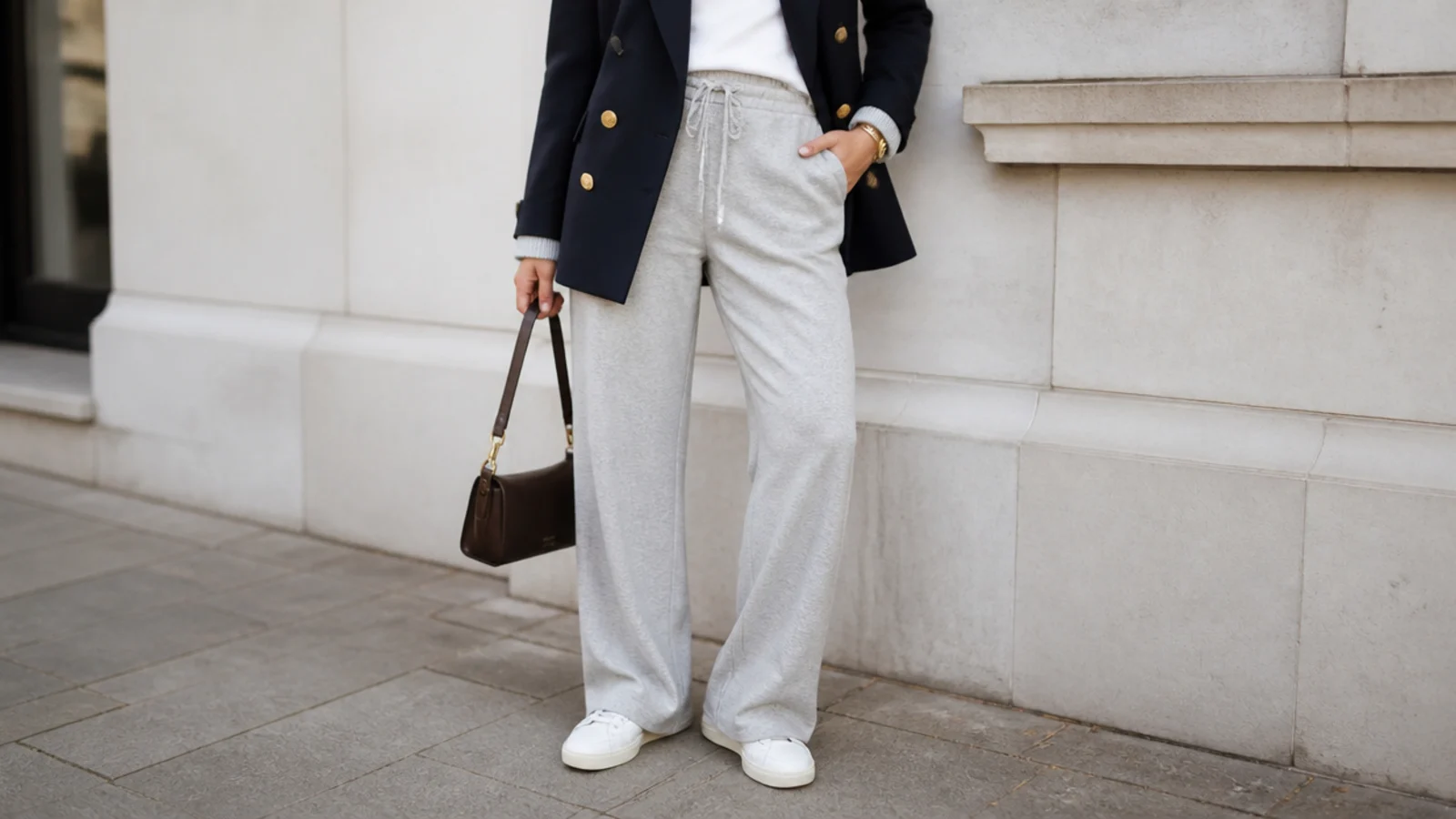 Faceless waist-down shot of straight-leg gray sweatpants with a navy double-breasted blazer and white sneakers
