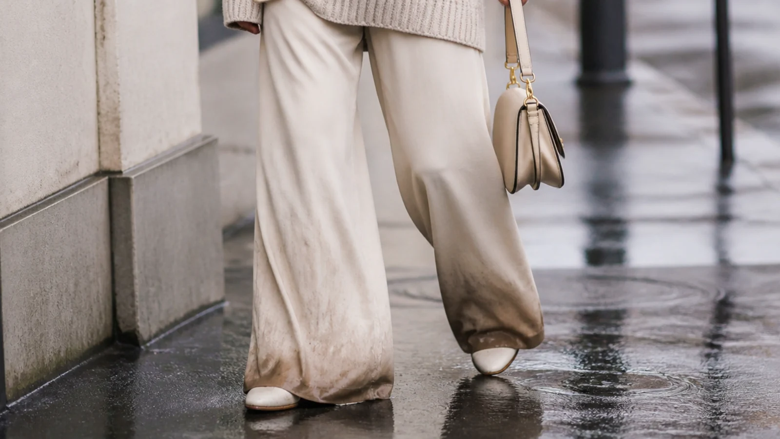 Faceless waist-down shot of wide-leg trousers with a soaked dragging hem in the rain as a mistake