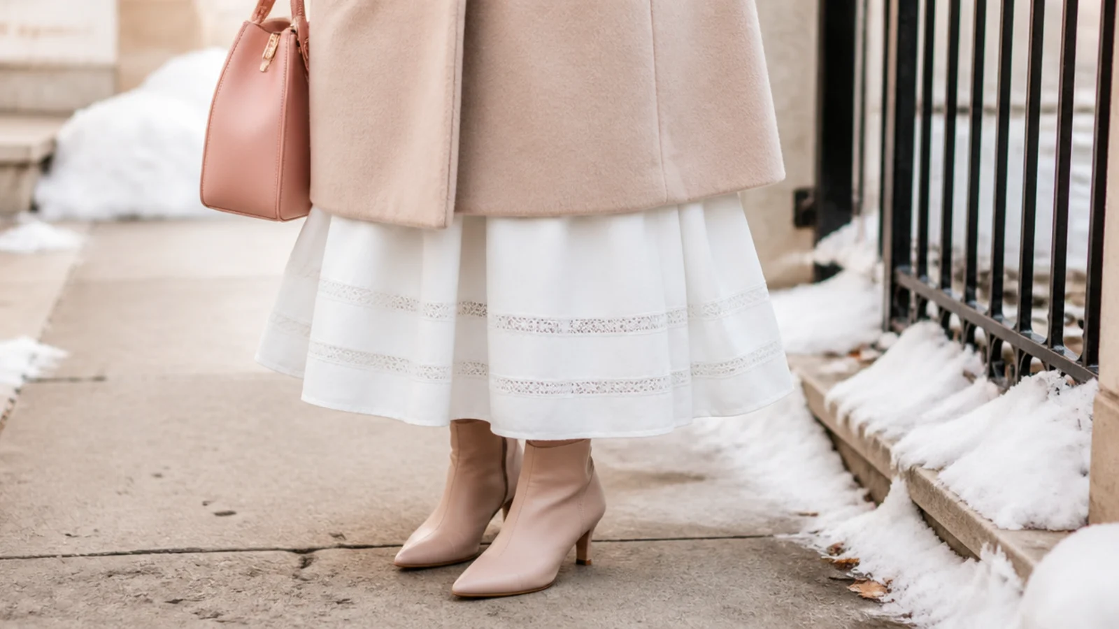 Faceless close-up of a white skirt hem kept clear of gray slush on a salted winter sidewalk