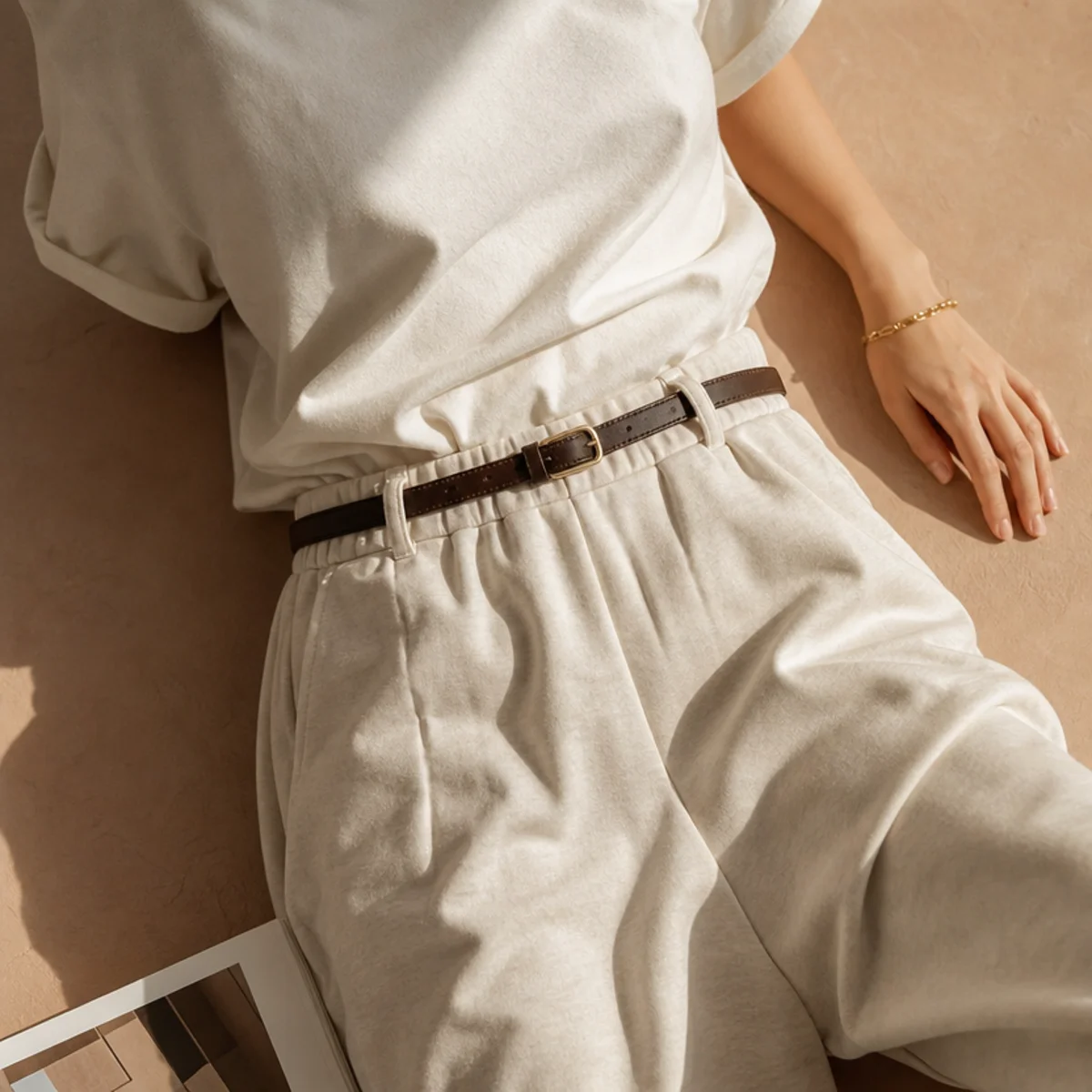 Faceless waist-up shot of a tucked tee with a slim belt over baggy high-waisted sweatpants