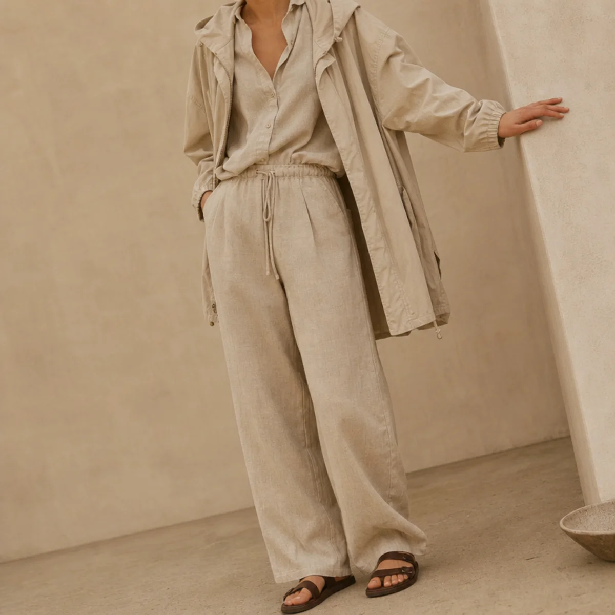 Faceless waist-up shot of a linen-blend set under a light anorak with sandals for summer rain