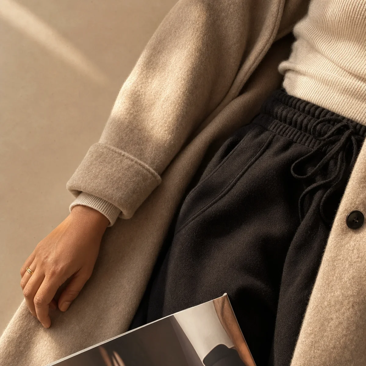 Faceless full-length shot of a long wool coat worn open over black sweatpants and a knit top
