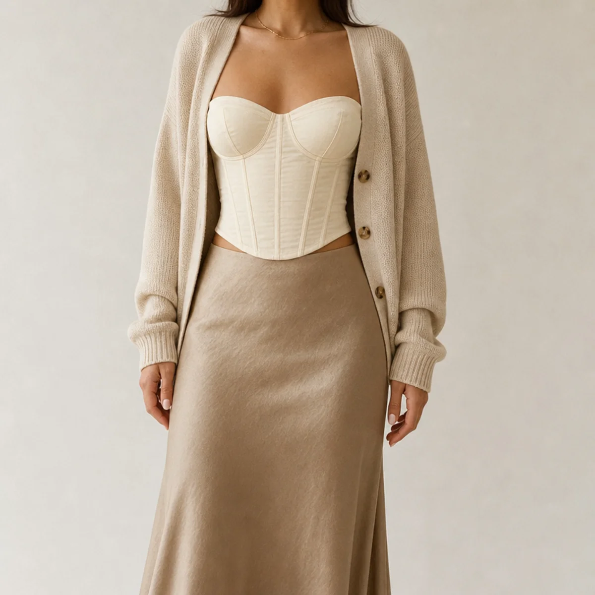 Faceless waist-up shot of a corset top under an open cardigan with a midi skirt