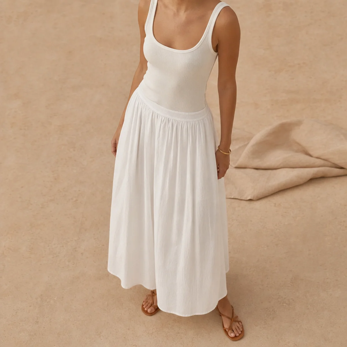 Faceless full-length shot of a flowing white maxi skirt with a fitted tank and flat sandals
