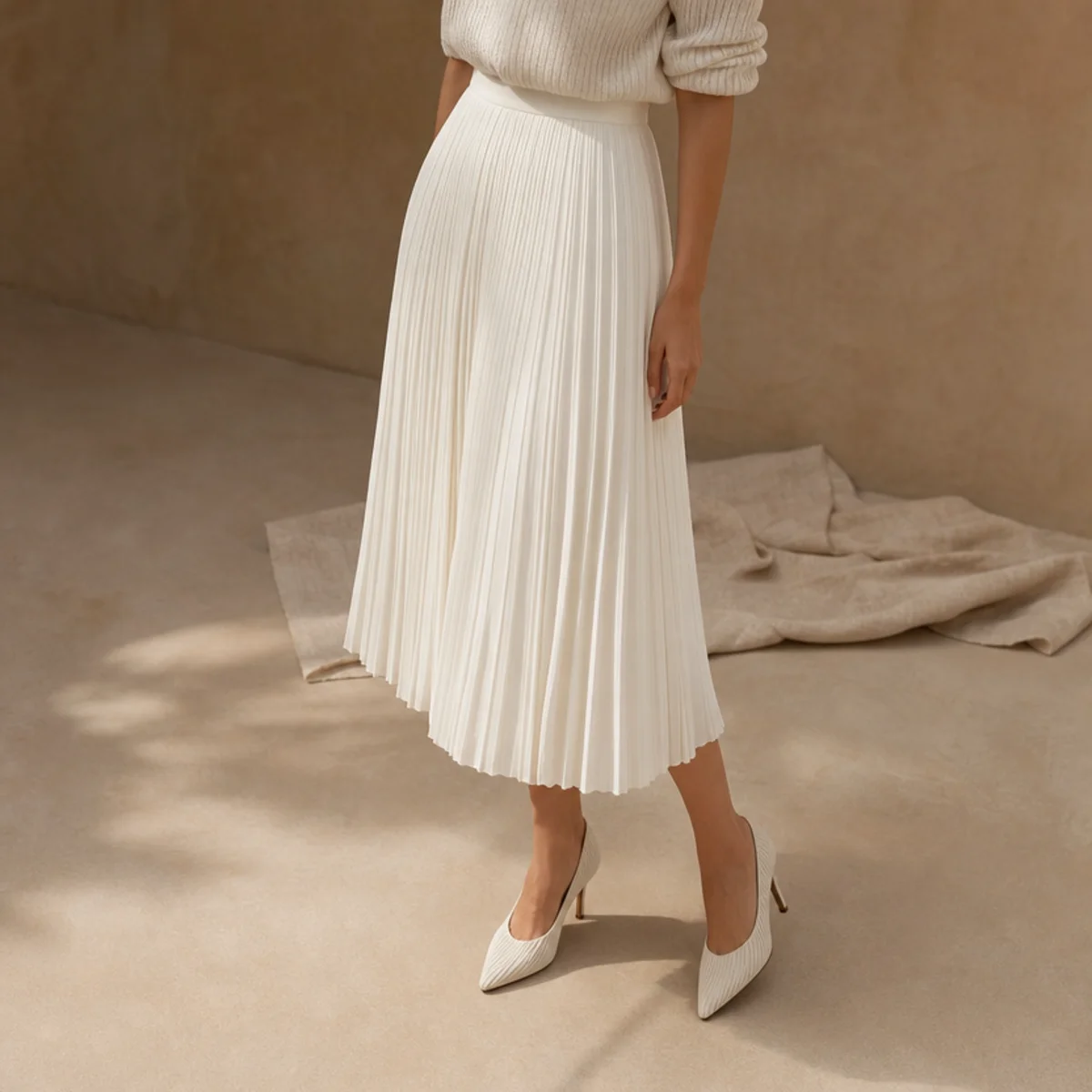 Faceless full-length shot of a white pleated midi skirt with a tucked knit and heels