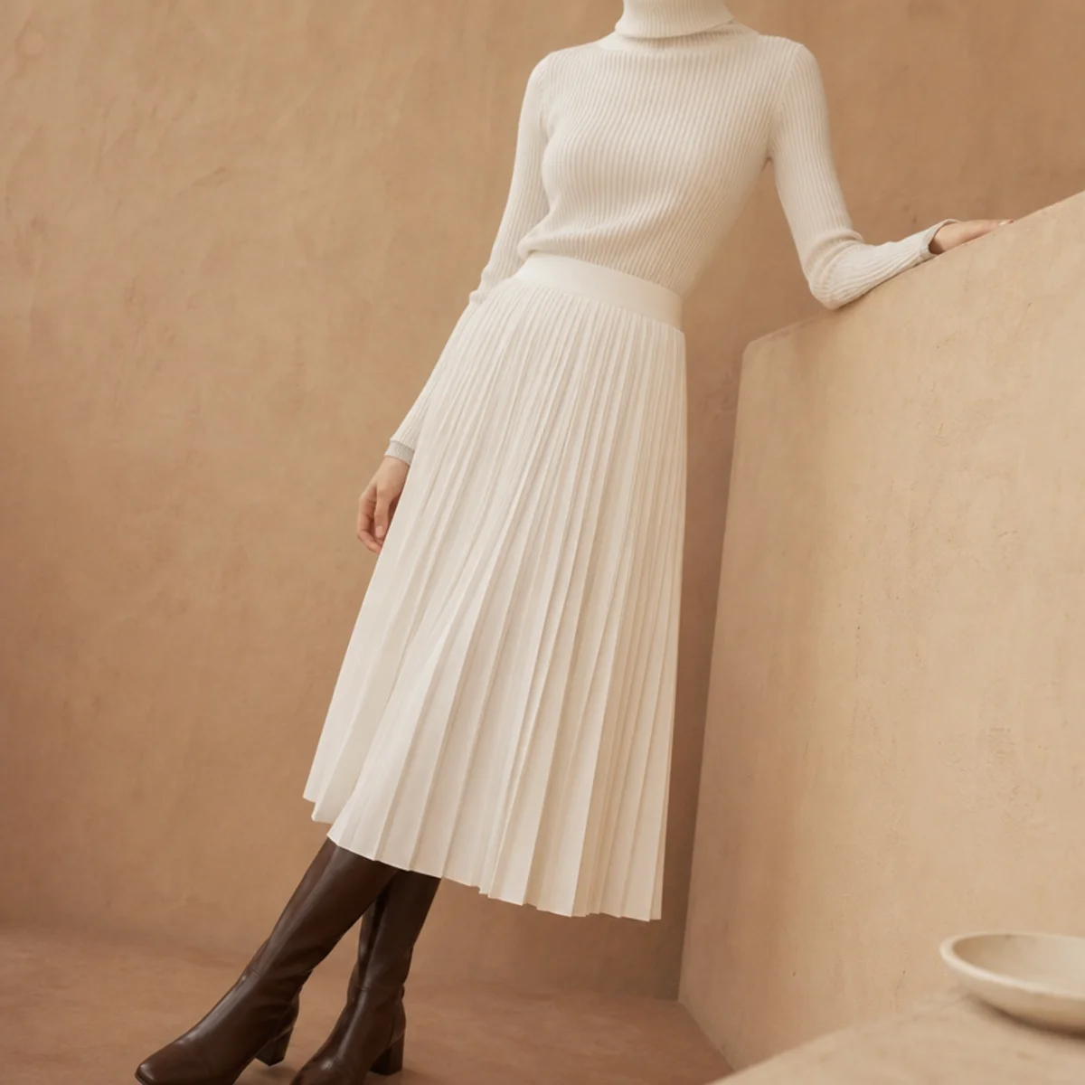 Faceless waist-up shot of a white pleated skirt with a fitted turtleneck and boots