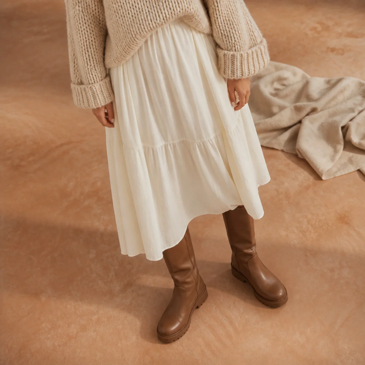 Faceless full-length shot of a white skirt with a chunky knit and tall boots