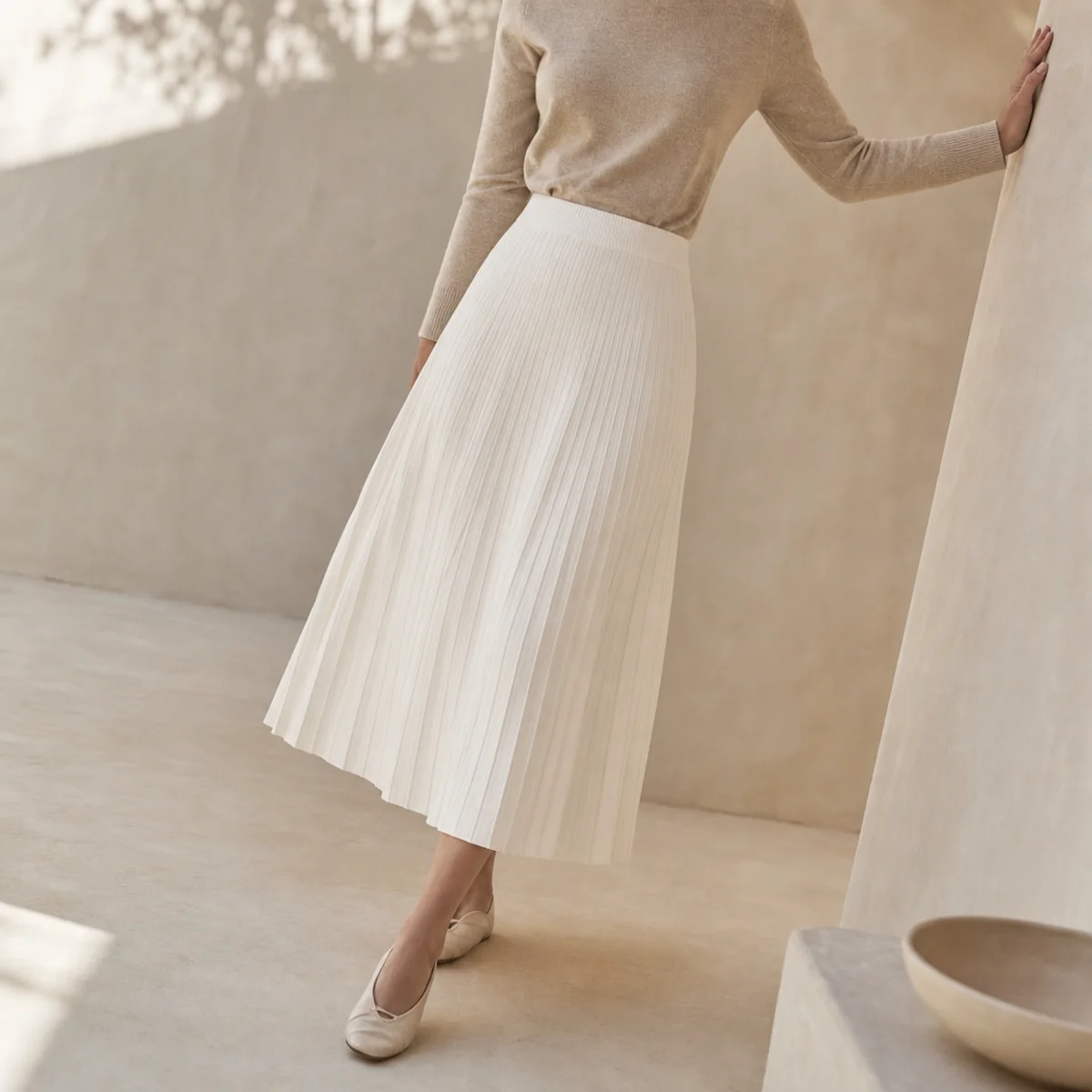 Faceless full-length shot of a white pleated midi skirt with a tucked knit and flats