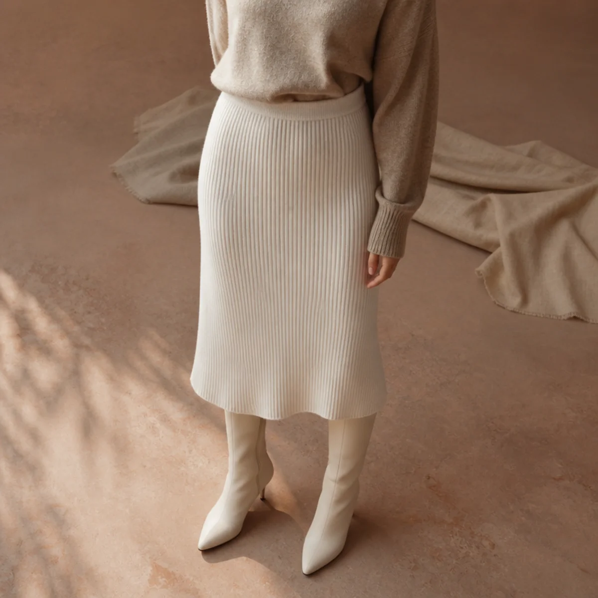 Faceless full-length shot of a white midi skirt with a tucked knit and tall boots